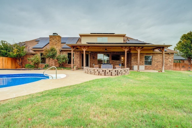 rear view of house with a fenced in pool, a lawn, a patio area, and solar panels