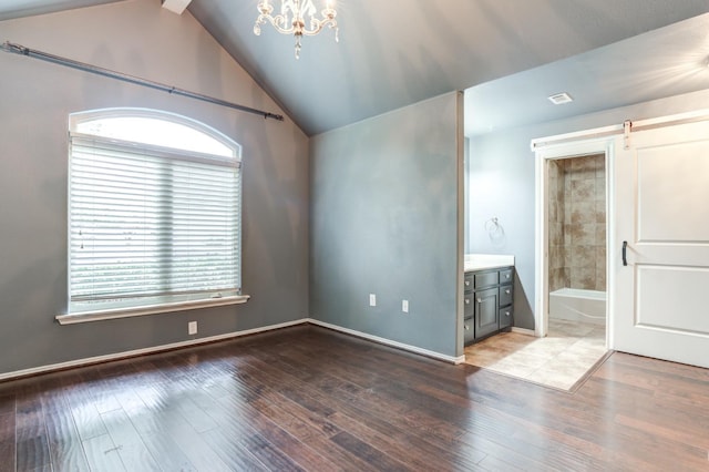 unfurnished room with wood-type flooring, a barn door, lofted ceiling, and a chandelier