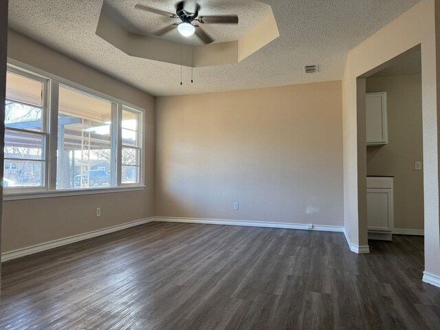 empty room with dark hardwood / wood-style flooring, a textured ceiling, a raised ceiling, and ceiling fan