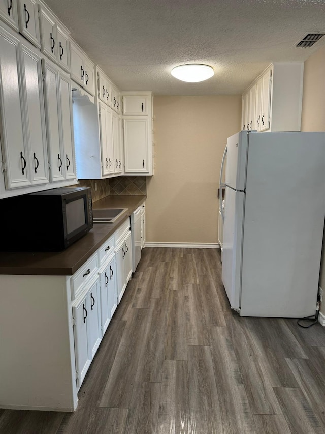 kitchen featuring dark hardwood / wood-style floors, white cabinets, decorative backsplash, white appliances, and a textured ceiling