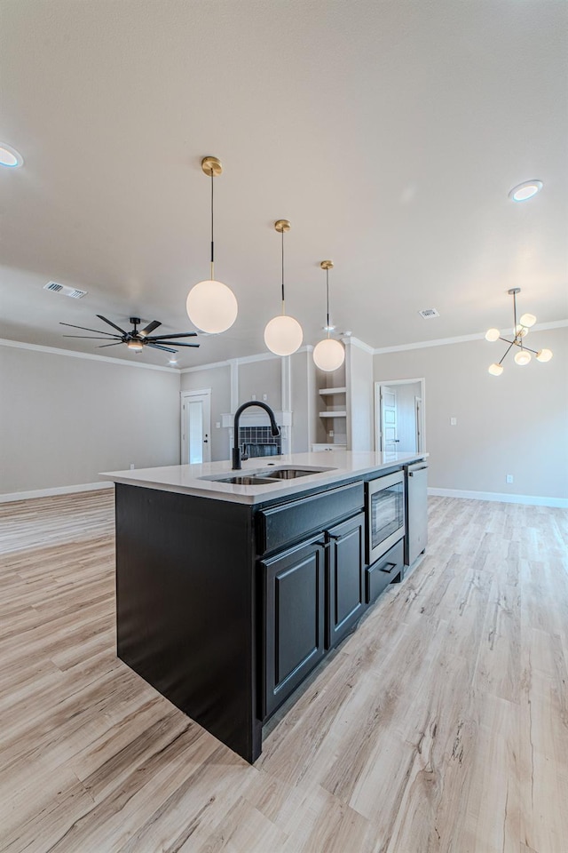 kitchen with stainless steel microwave, an island with sink, sink, hanging light fixtures, and crown molding