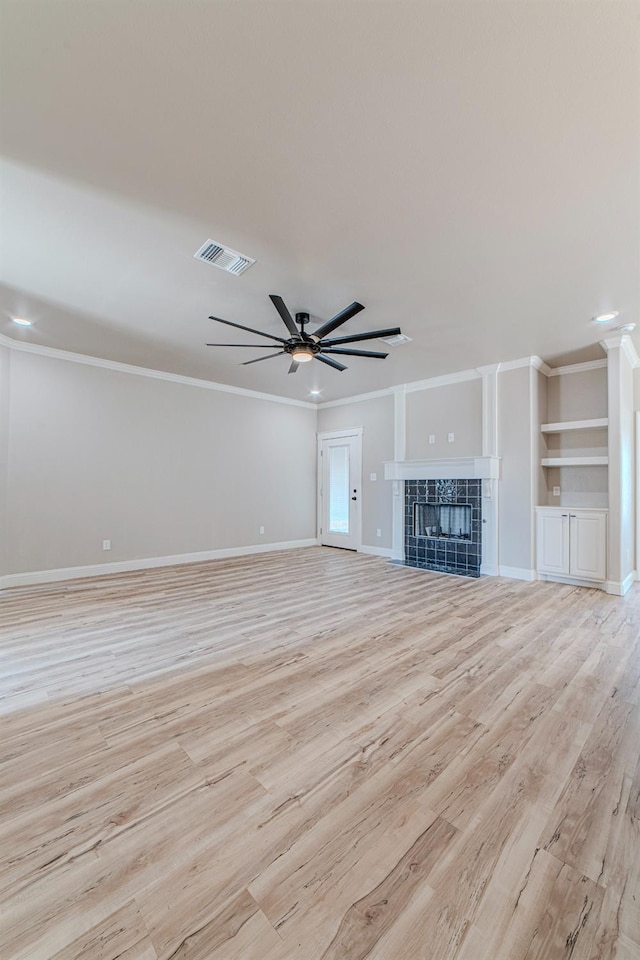 unfurnished living room featuring ceiling fan, crown molding, a fireplace, and built in shelves