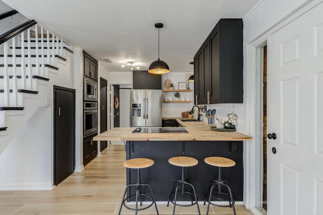 kitchen featuring a kitchen bar, butcher block counters, pendant lighting, stainless steel appliances, and light hardwood / wood-style floors