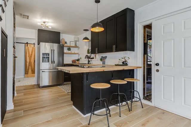 kitchen featuring stainless steel refrigerator with ice dispenser, wood counters, a breakfast bar area, hanging light fixtures, and a barn door