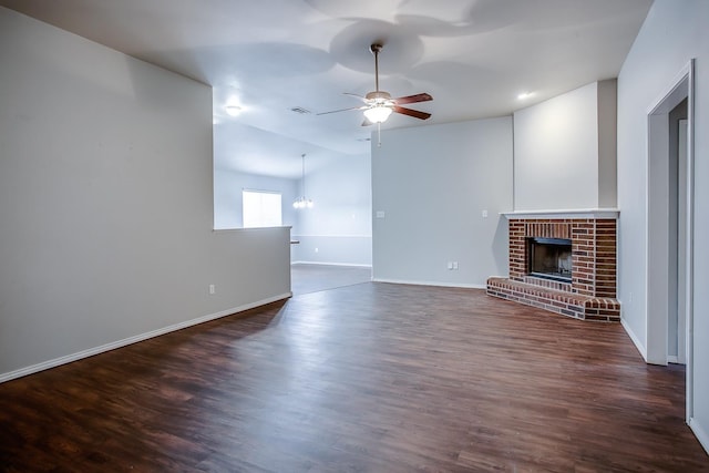 unfurnished living room featuring dark wood-type flooring, lofted ceiling, a fireplace, and ceiling fan with notable chandelier