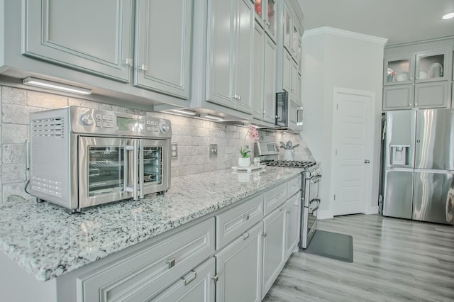 kitchen with light stone counters, light hardwood / wood-style flooring, ornamental molding, stainless steel appliances, and decorative backsplash