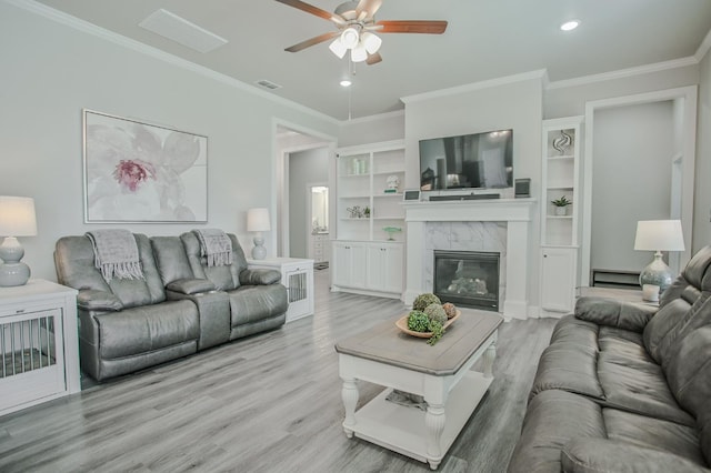 living room featuring crown molding, a premium fireplace, ceiling fan, and light wood-type flooring