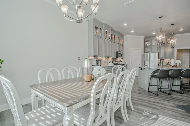 dining area featuring crown molding, an inviting chandelier, and light hardwood / wood-style floors