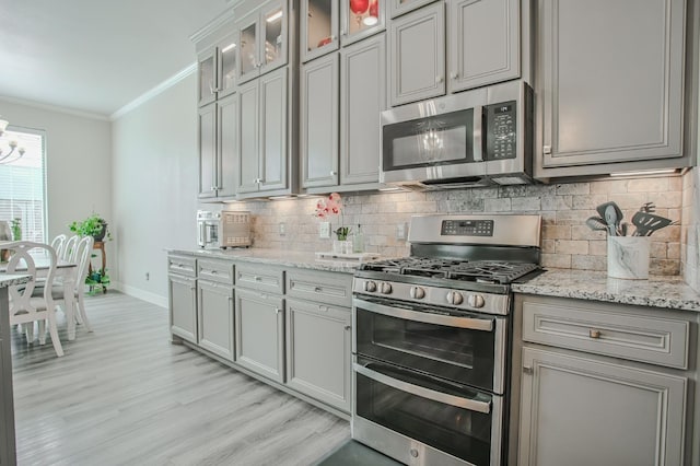 kitchen with stainless steel appliances, ornamental molding, light stone countertops, and backsplash