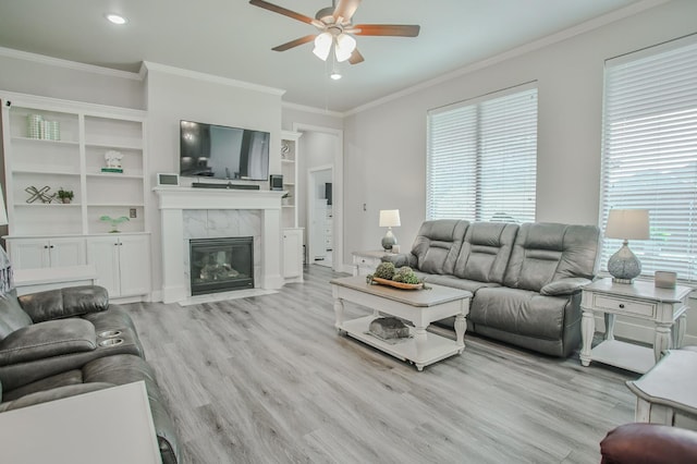 living room with a tiled fireplace, ornamental molding, ceiling fan, and light wood-type flooring