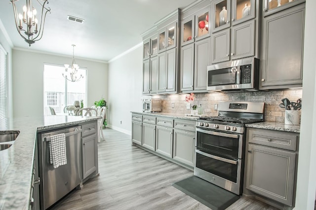 kitchen featuring pendant lighting, light stone countertops, stainless steel appliances, and an inviting chandelier