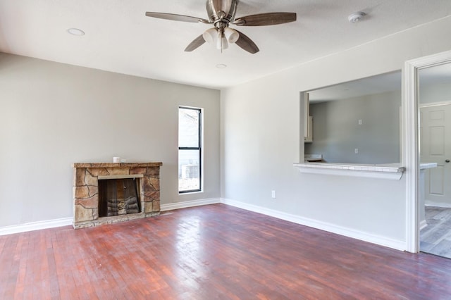 unfurnished living room with hardwood / wood-style flooring, a stone fireplace, and ceiling fan