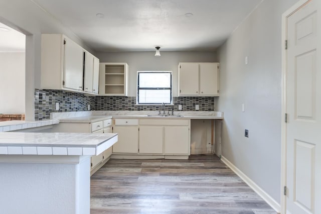 kitchen featuring sink, light hardwood / wood-style floors, decorative backsplash, tile countertops, and kitchen peninsula