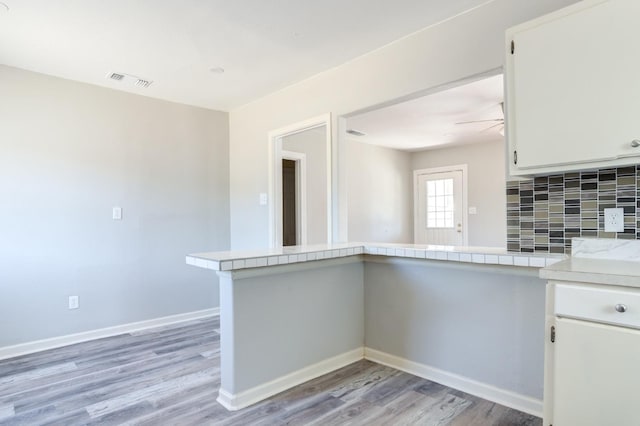 kitchen featuring tasteful backsplash, light hardwood / wood-style floors, kitchen peninsula, and white cabinets