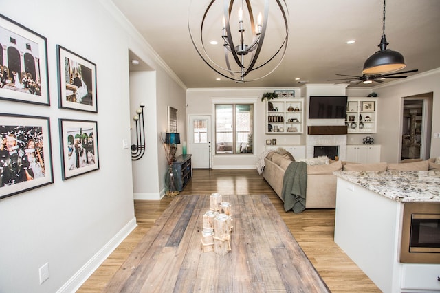 living room with light wood-style floors, baseboards, ornamental molding, a fireplace, and ceiling fan with notable chandelier
