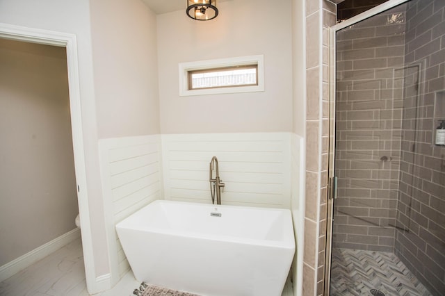 bathroom featuring toilet, a soaking tub, a wainscoted wall, and a stall shower