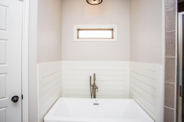 full bathroom with a freestanding tub, a sink, and wainscoting