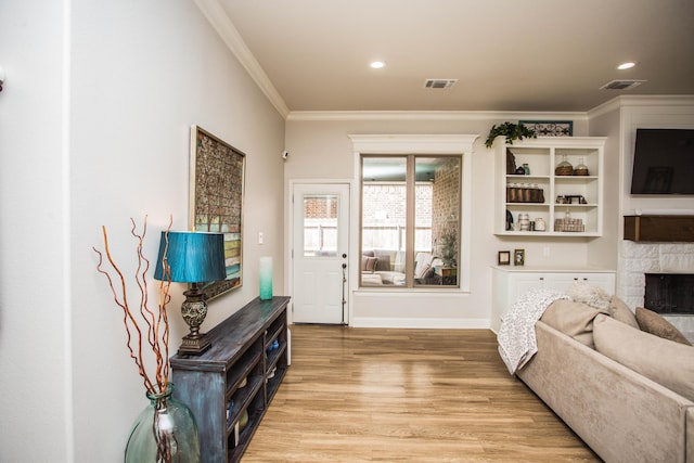living area with crown molding, a stone fireplace, visible vents, light wood-style flooring, and baseboards