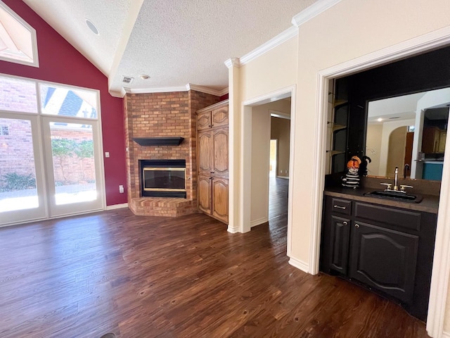 unfurnished living room with sink, a fireplace, a textured ceiling, dark hardwood / wood-style flooring, and vaulted ceiling