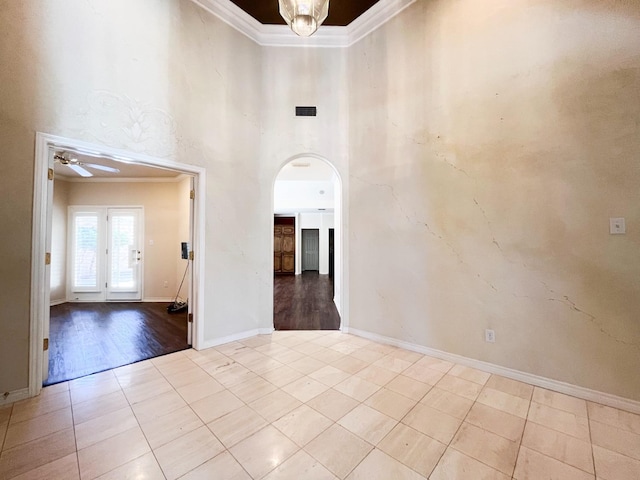 empty room featuring light tile patterned flooring, ceiling fan, ornamental molding, and a high ceiling