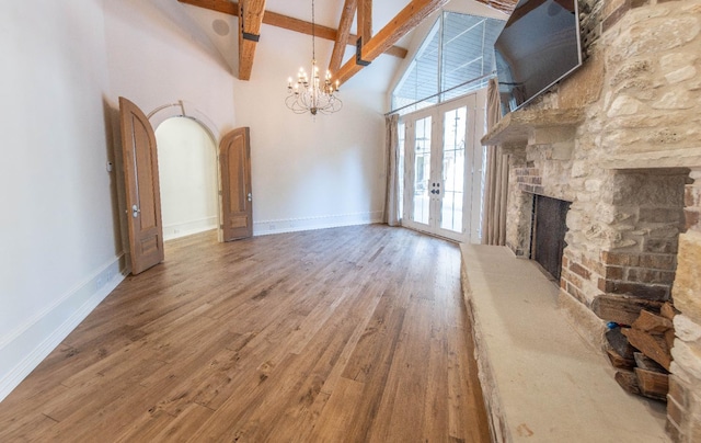 unfurnished living room with high vaulted ceiling, a fireplace, wood-type flooring, beam ceiling, and an inviting chandelier