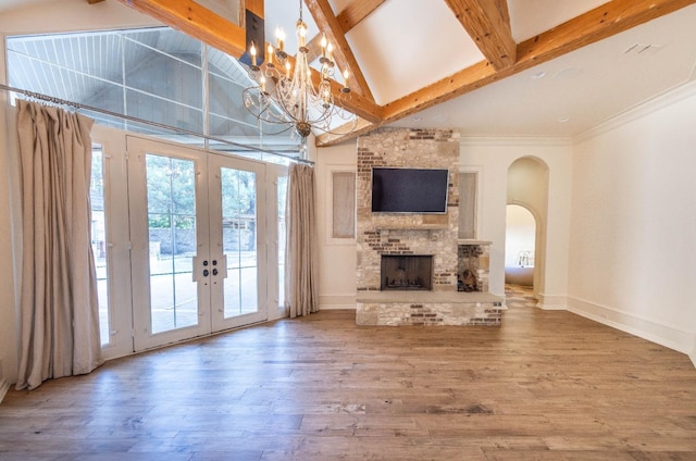 unfurnished living room with french doors, an inviting chandelier, wood-type flooring, a large fireplace, and beamed ceiling