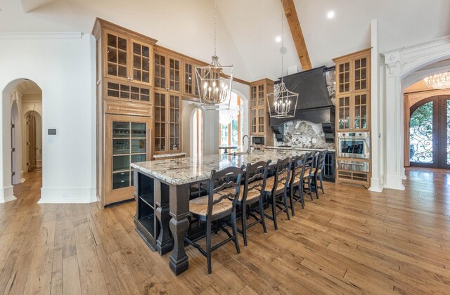 kitchen featuring a spacious island, an inviting chandelier, light stone counters, custom range hood, and oven