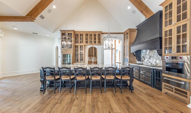 kitchen with pendant lighting, light stone countertops, custom exhaust hood, stainless steel oven, and light wood-type flooring