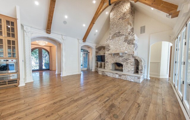 unfurnished living room featuring french doors, a fireplace, beam ceiling, and high vaulted ceiling