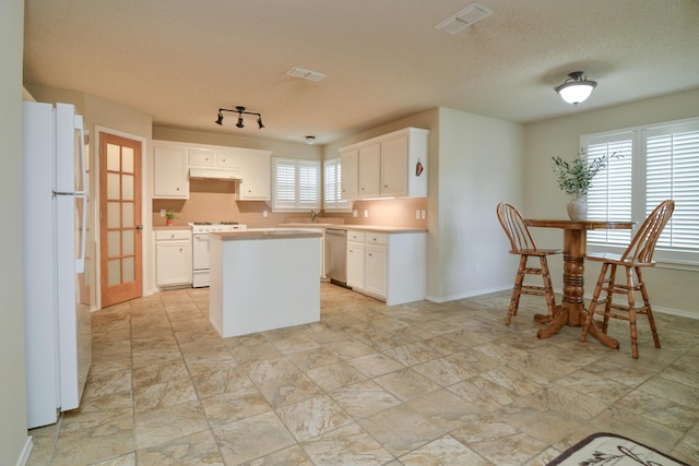 9808 Huron Ave, Lubbock, TX 79424 - kitchen with white appliances, a kitchen island, light countertops, white cabinets, and a textured ceiling