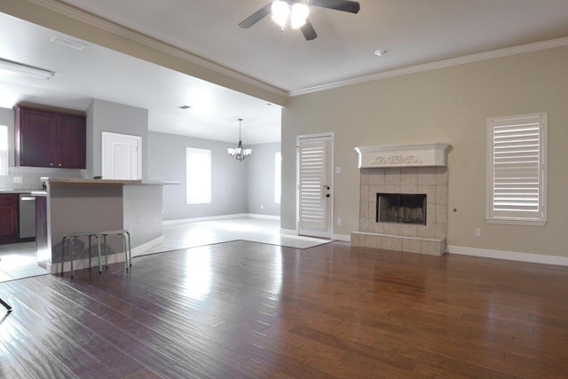 unfurnished living room with a tile fireplace, dark wood-type flooring, ceiling fan with notable chandelier, and ornamental molding