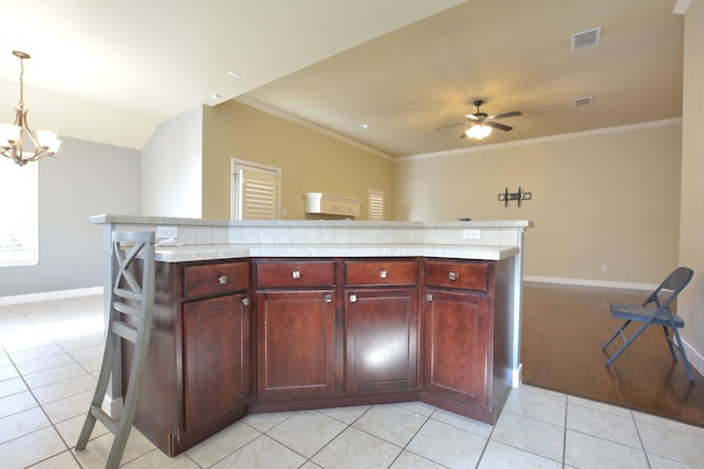 kitchen featuring light tile patterned flooring, a kitchen island, ceiling fan with notable chandelier, decorative light fixtures, and ornamental molding