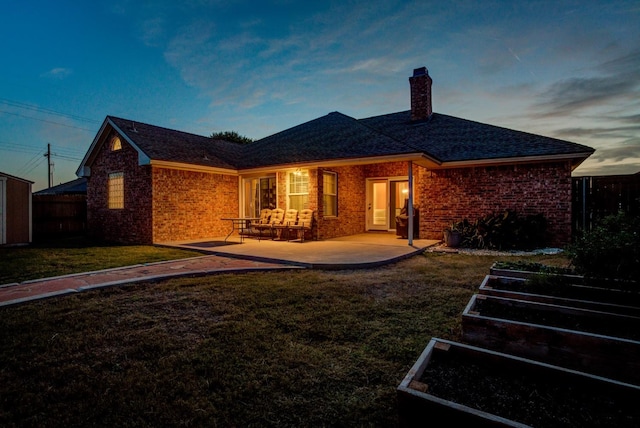 back house at dusk featuring a lawn and a patio area