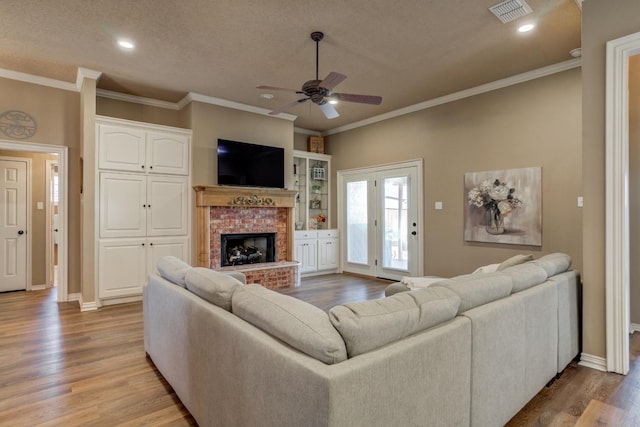 living room with crown molding, ceiling fan, a brick fireplace, and light hardwood / wood-style flooring