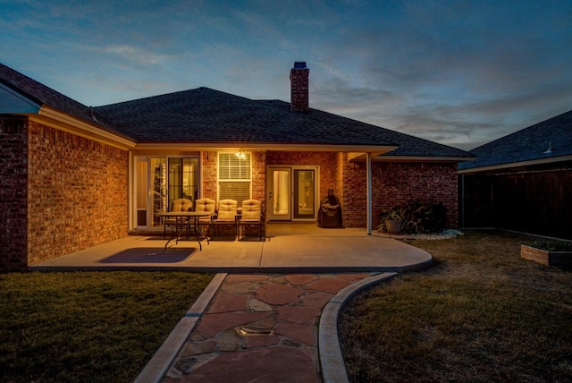 back house at dusk with a patio, an outdoor hangout area, and a lawn