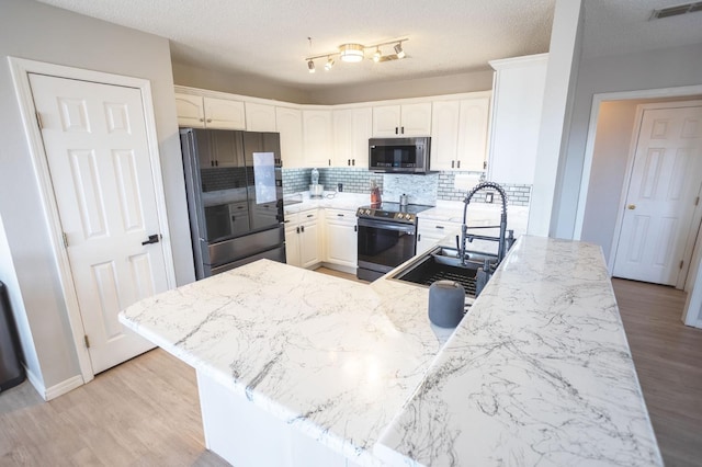 kitchen featuring appliances with stainless steel finishes, sink, white cabinets, kitchen peninsula, and light hardwood / wood-style flooring