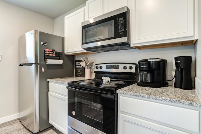 kitchen with appliances with stainless steel finishes, white cabinets, light stone counters, and light hardwood / wood-style floors