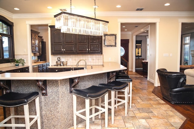 kitchen with crown molding, dark brown cabinetry, a kitchen breakfast bar, and decorative backsplash