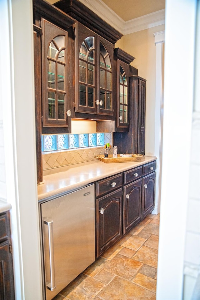 bar with dark brown cabinetry, decorative backsplash, ornamental molding, and built in fridge