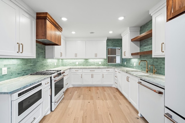 kitchen featuring tasteful backsplash, white cabinetry, sink, light wood-type flooring, and white appliances