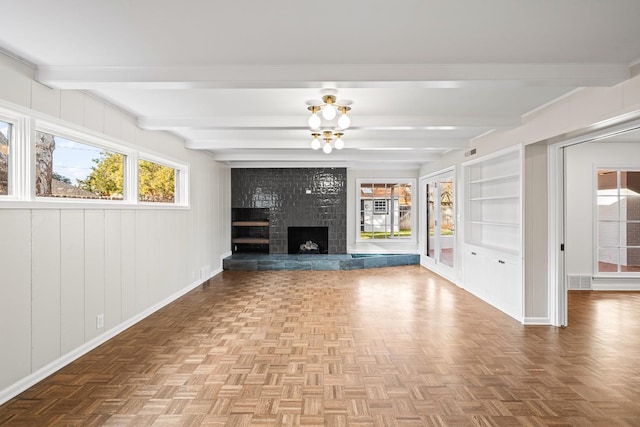 unfurnished living room featuring beamed ceiling, parquet flooring, a fireplace, and built in features