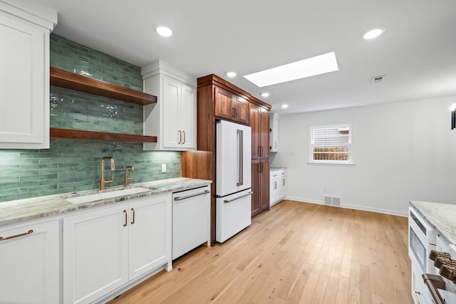 kitchen with sink, white appliances, a skylight, and white cabinets