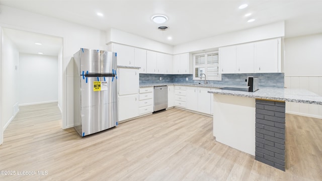 3811 42nd St, Lubbock, TX 79413 - kitchen with stainless steel appliances, a peninsula, light wood-style floors, white cabinets, and tasteful backsplash