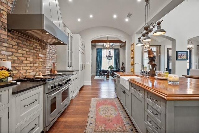 kitchen featuring wall chimney range hood, wooden counters, hanging light fixtures, double oven range, and a notable chandelier