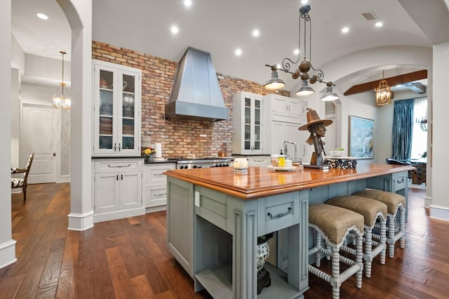 kitchen with a kitchen island, butcher block counters, white cabinets, and custom range hood