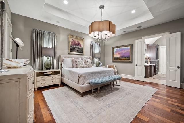 bedroom featuring an inviting chandelier, a tray ceiling, and dark hardwood / wood-style floors