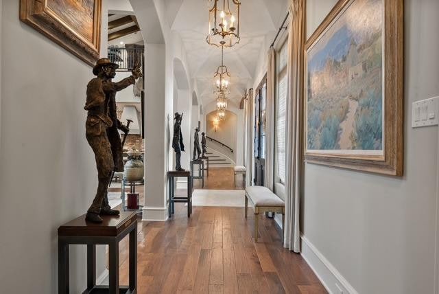 corridor with beamed ceiling, hardwood / wood-style floors, and a notable chandelier