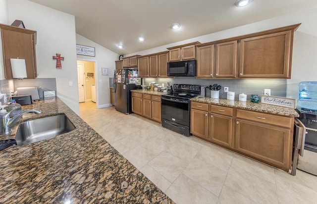 kitchen featuring vaulted ceiling, dark stone counters, sink, and black appliances