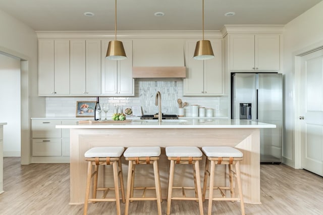 kitchen featuring pendant lighting, an island with sink, sink, backsplash, and stainless steel refrigerator with ice dispenser