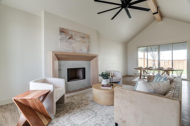 living room with a tiled fireplace, vaulted ceiling with beams, light hardwood / wood-style flooring, and ceiling fan